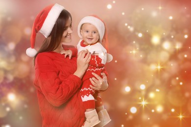 Image of Happy mother with cute baby in Christmas outfits and Santa hats on red background, space for text. Magical festive atmosphere