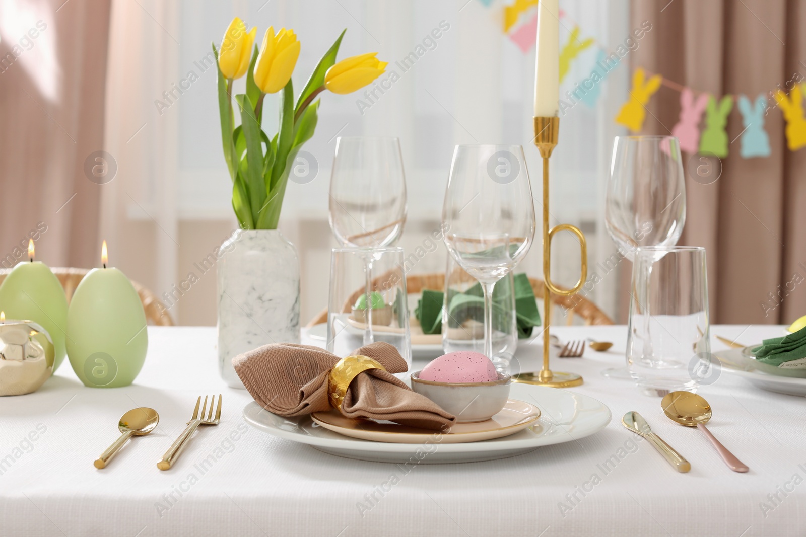 Photo of Festive Easter table setting with painted eggs, burning candles and yellow tulips indoors