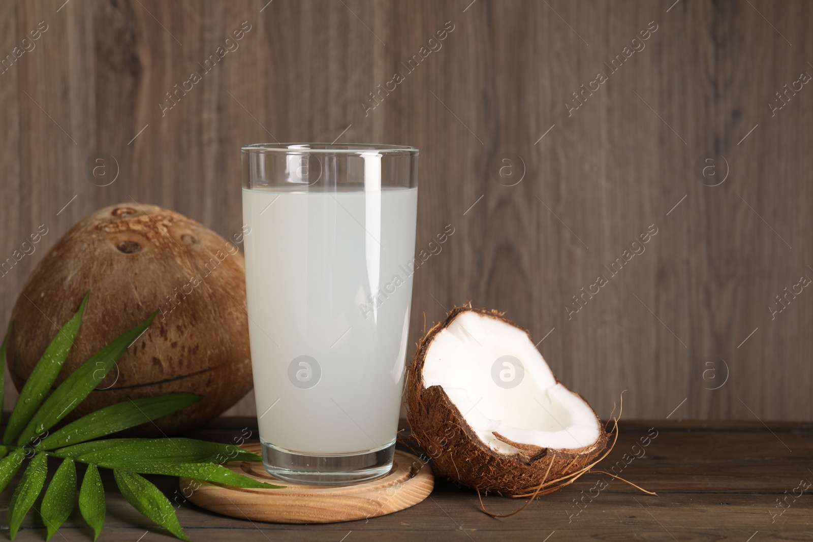 Photo of Glass of coconut water, leaf and nuts on wooden table, space for text