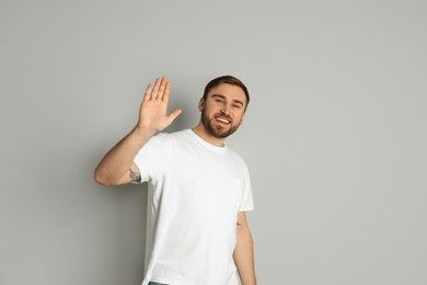 Photo of Happy young man waving to say hello on light grey background