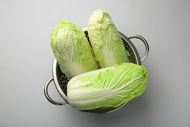 Photo of Fresh Chinese cabbages in colander on light background, top view