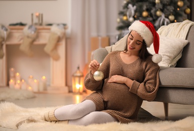 Happy pregnant woman with Christmas ball at home. Expecting baby