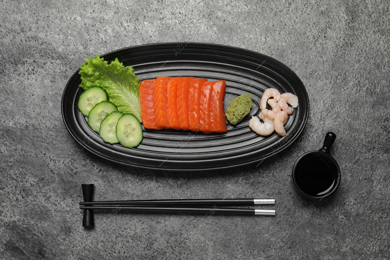 Photo of Tasty salmon slices, shrimp, cucumber and lettuce on grey table, flat lay. Delicious sashimi dish