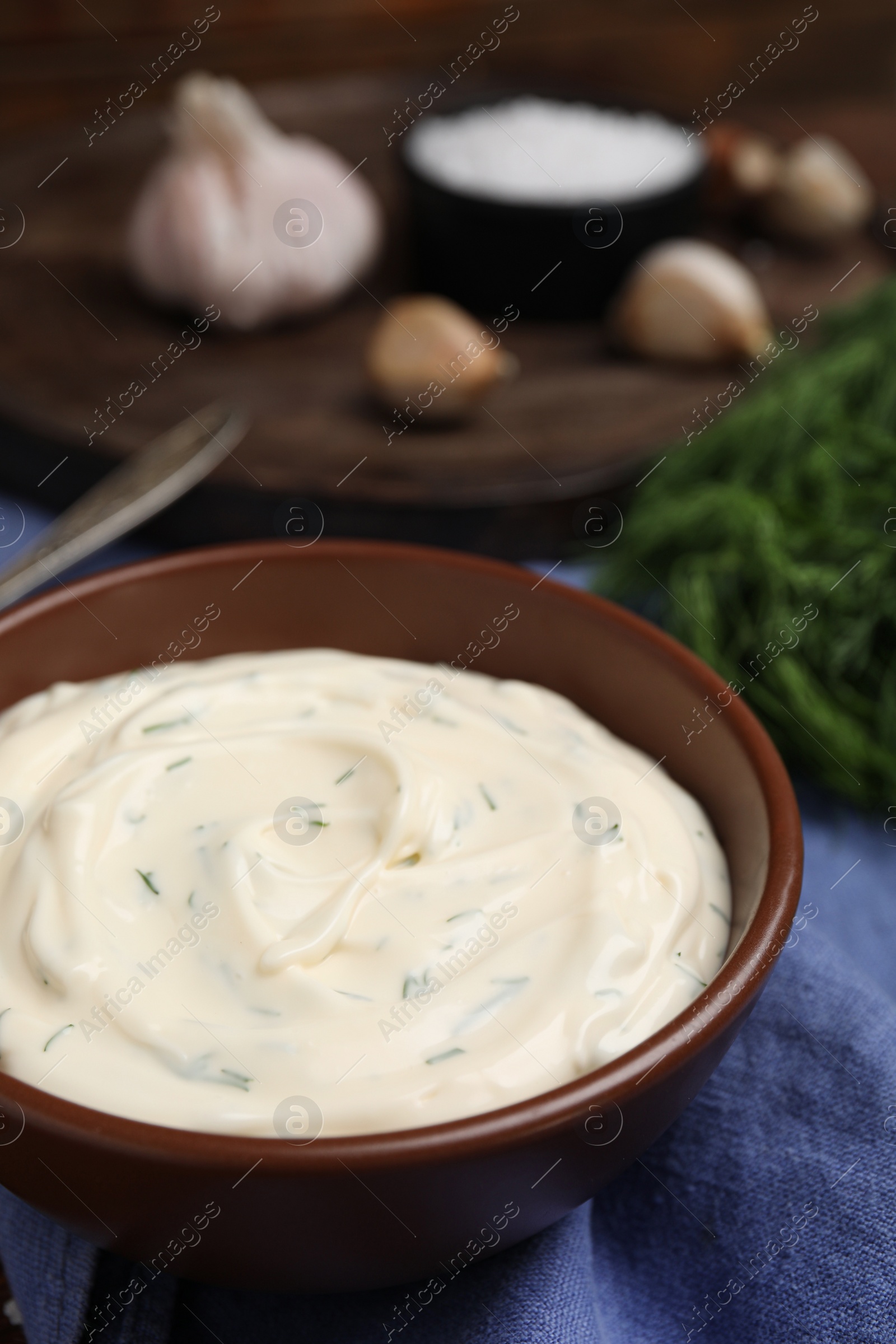 Photo of Tasty creamy dill sauce in bowl on blue kitchen towel, closeup