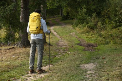 Man with backpack and trekking poles on trail, space for text. Tourism equipment