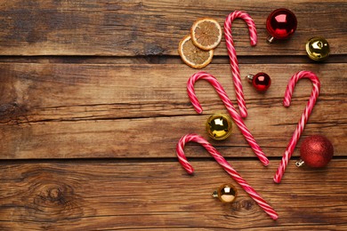 Tasty candy canes, Christmas balls and dried orange slices on wooden table, flat lay. Space for text