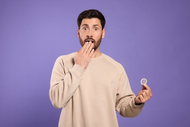 Man holding condom on purple background. Safe sex