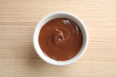 Photo of Bowl with sweet chocolate cream on wooden background, top view