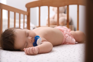 Photo of Cute little baby with pacifier sleeping in crib at home