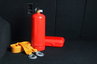 Photo of Fire extinguisher, towing strap and first aid kit in trunk, space for text. Car safety equipment