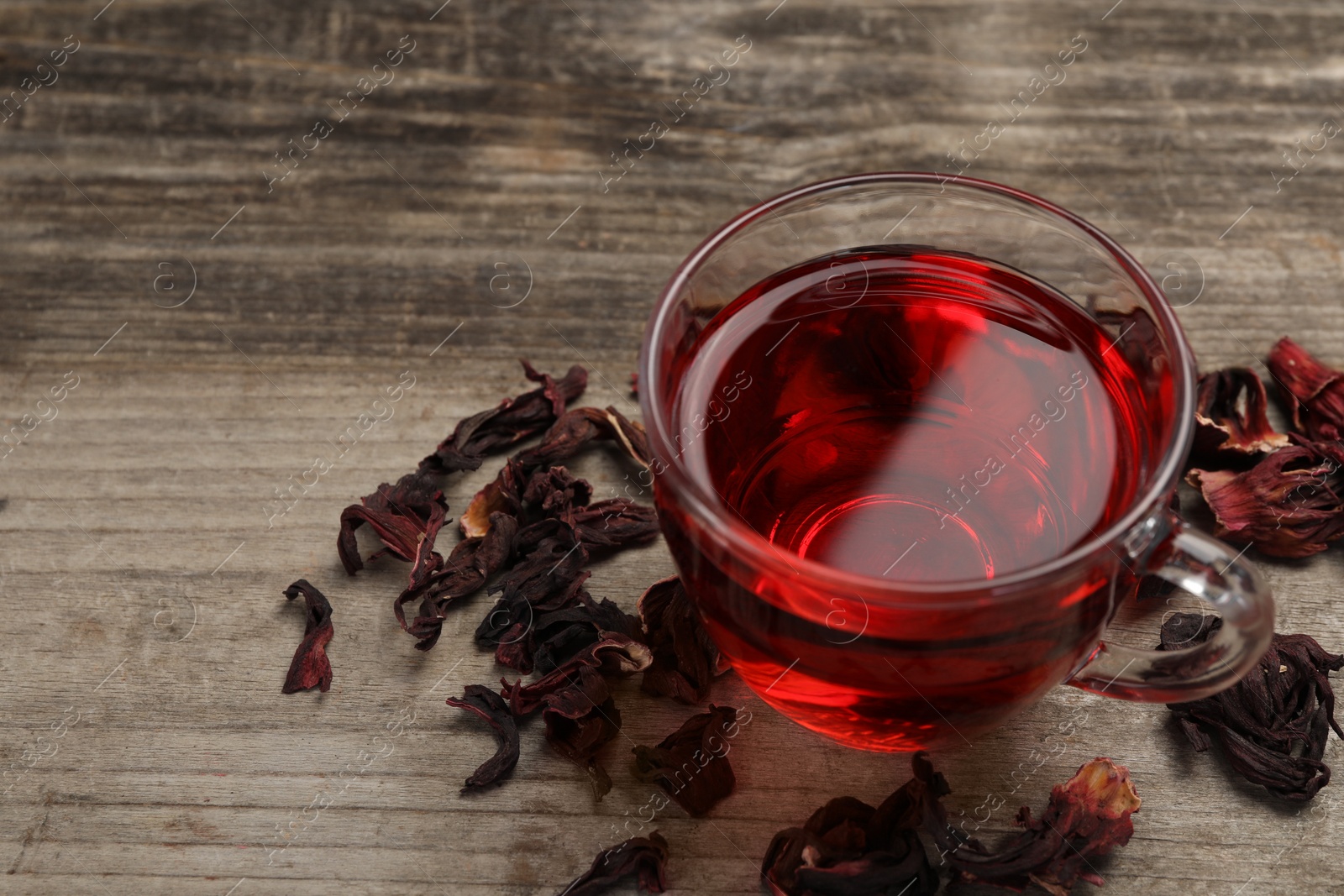 Photo of Cup of fresh hibiscus tea and dry flower leaves on wooden table. Space for text