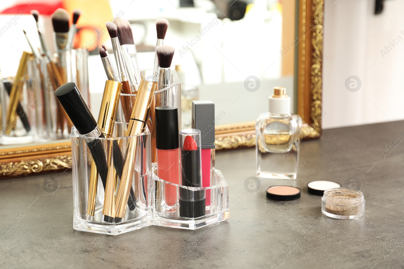 Photo of Lipstick holder with different makeup products on dressing table near mirror. Space for text