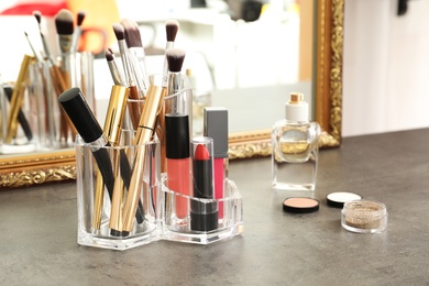 Photo of Lipstick holder with different makeup products on dressing table near mirror. Space for text