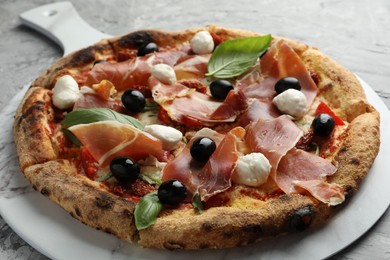 Photo of Tasty pizza with cured ham, olives, mozzarella cheese, sun-dried tomato and basil on gray table, closeup