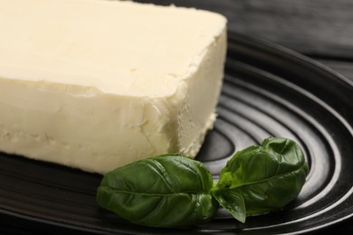 Photo of Block of tasty butter and basil on black table, closeup