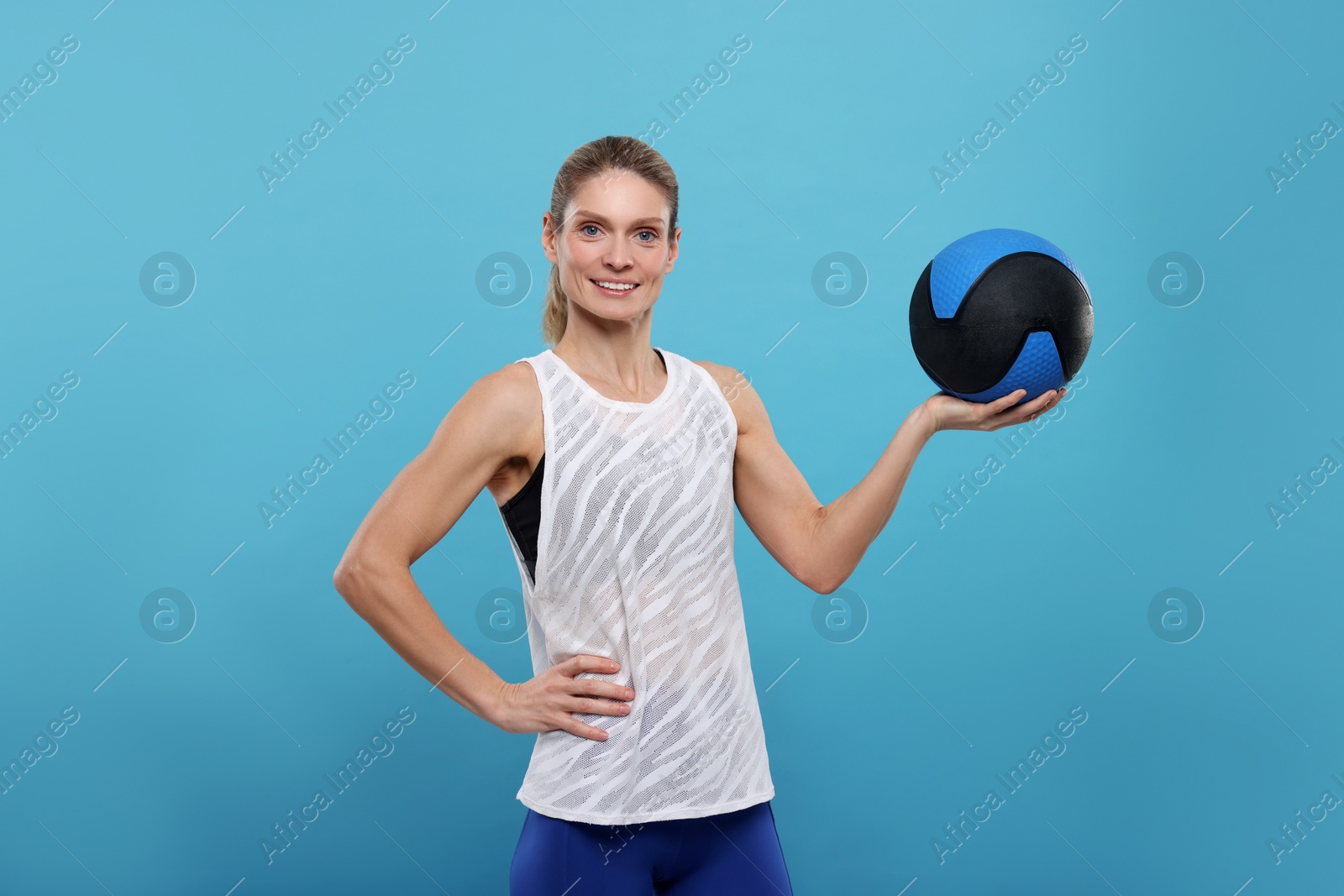 Photo of Portrait of happy sportswoman with medicine ball on light blue background