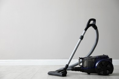 Photo of Modern vacuum cleaner near white wall indoors, space for text