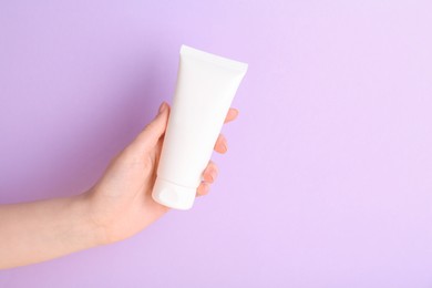 Woman with tube of cream on lilac background, closeup