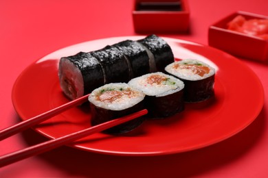 Photo of Tasty sushi rolls and chopsticks on red background, closeup