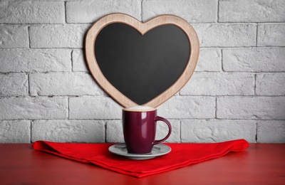 Photo of Cup of coffee on table near heart shaped chalkboard