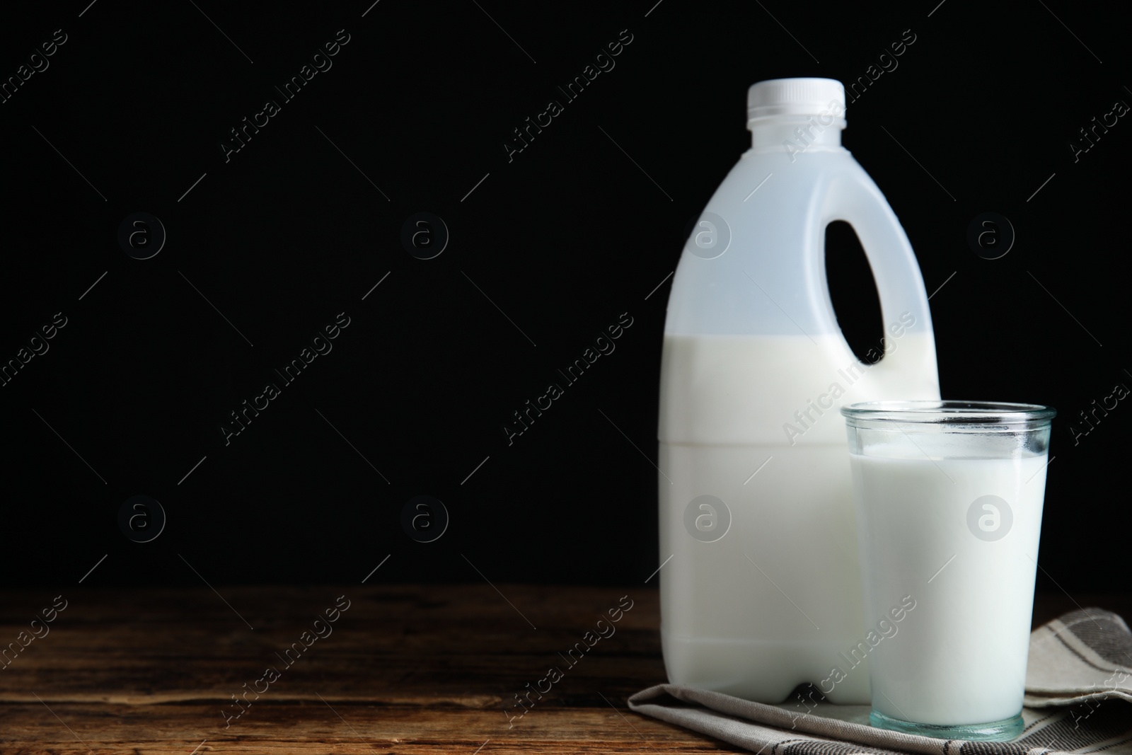 Photo of Gallon bottle and glass of milk on wooden table, space for text