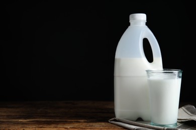 Photo of Gallon bottle and glass of milk on wooden table, space for text