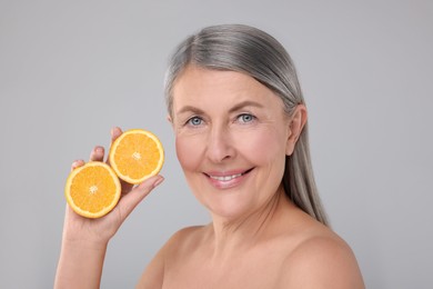 Photo of Beautiful woman with halves of orange rich in vitamin C on grey background