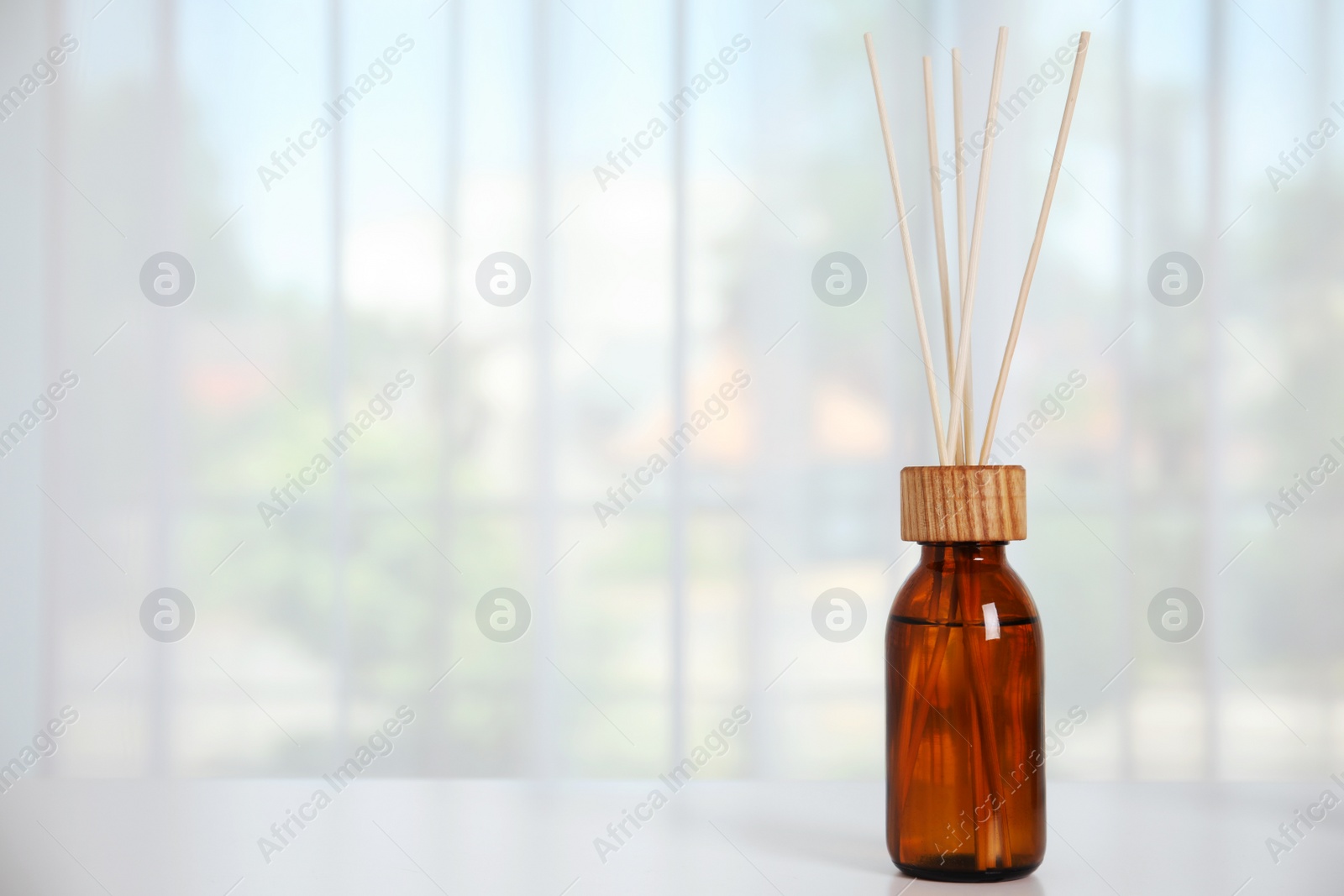 Photo of Reed diffuser on white table against window in room. Space for text