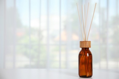 Photo of Reed diffuser on white table against window in room. Space for text