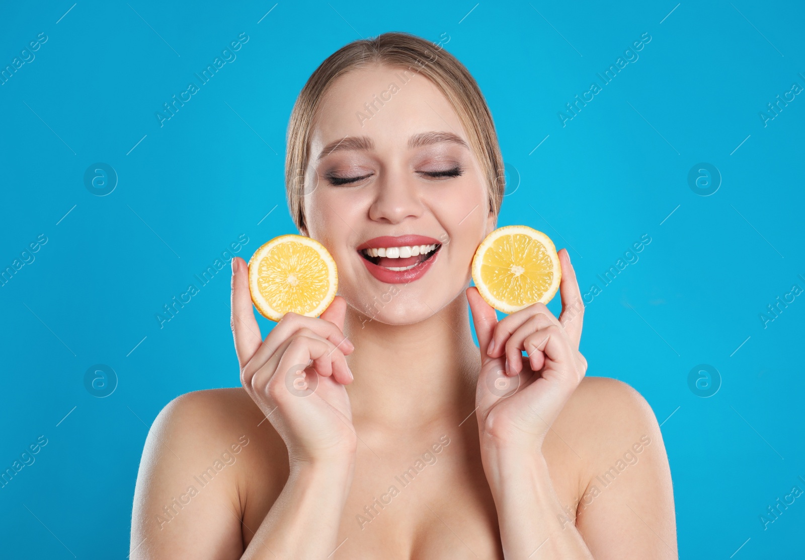 Photo of Young woman with cut lemon on blue background. Vitamin rich food