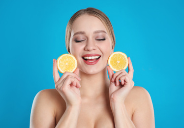 Photo of Young woman with cut lemon on blue background. Vitamin rich food