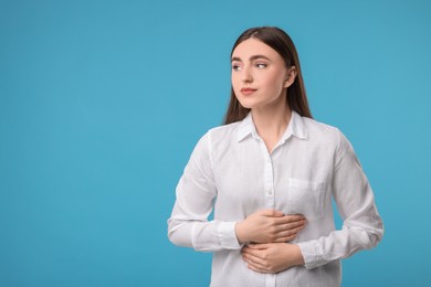 Photo of Young woman suffering from stomach pain on light blue background. Space for text