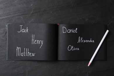 Photo of Notebook with written different baby names and pencil on black table, flat lay