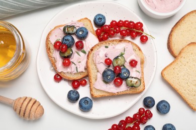 Photo of Tasty sandwiches with cream cheese, berries and honey on white table, flat lay