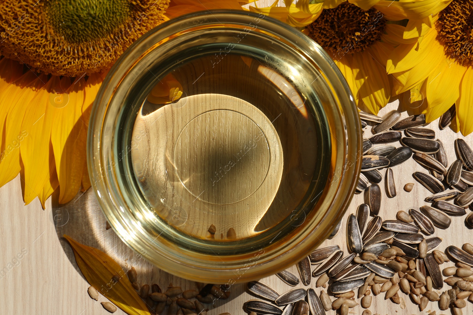 Photo of Sunflower oil in glass bowl and seeds on wooden table, flat lay