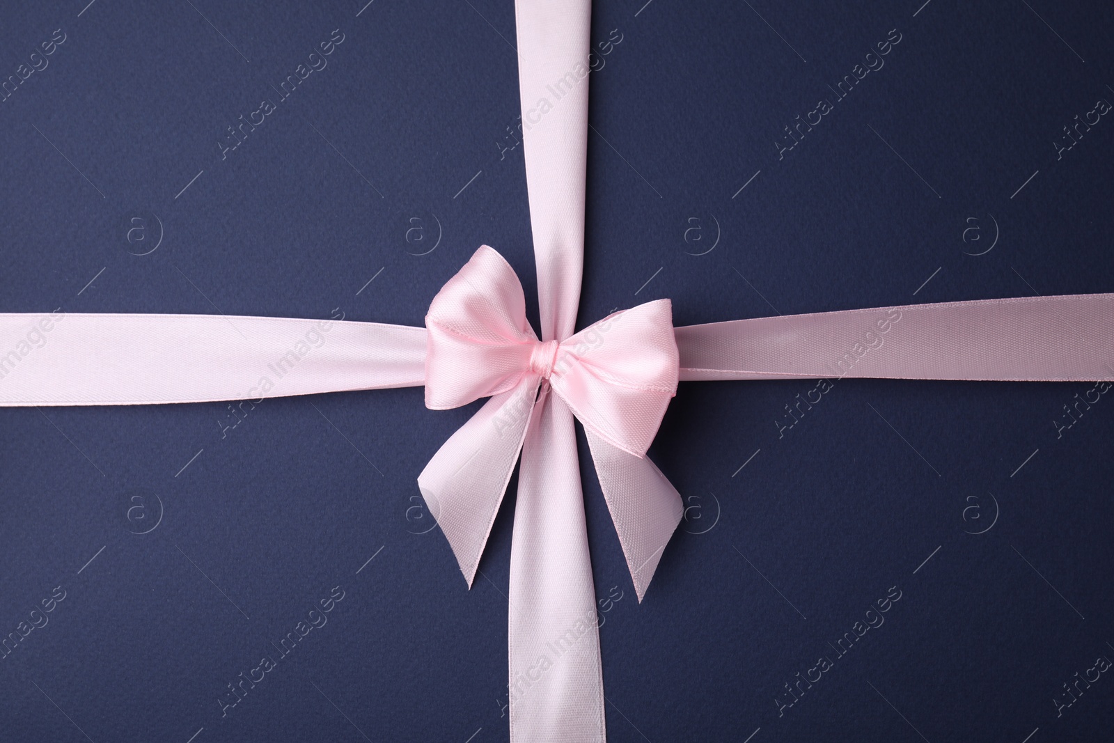 Photo of Pink satin ribbon with bow on blue background, top view