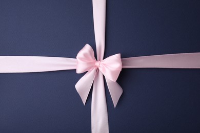 Pink satin ribbon with bow on blue background, top view