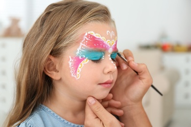 Artist painting face of little girl indoors