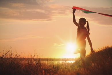 Photo of Cute little child with kite running outdoors at sunset. Spending time in nature
