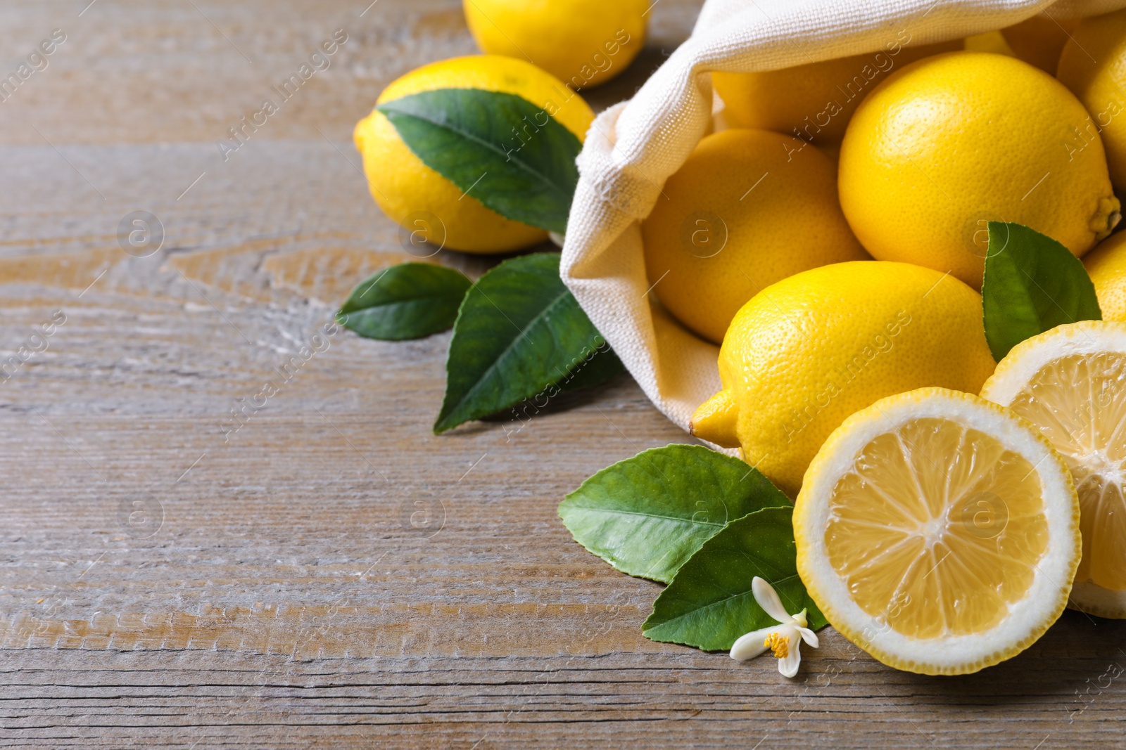 Photo of Many fresh ripe lemons with green leaves and flower on wooden table, closeup. Space for text