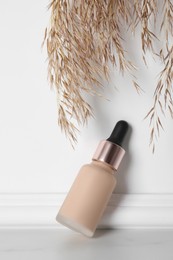 Photo of Skin foundation and decorative plant near white wall. Makeup product