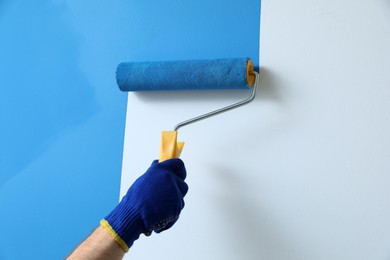 Photo of Man applying light blue paint with roller brush on white wall, closeup