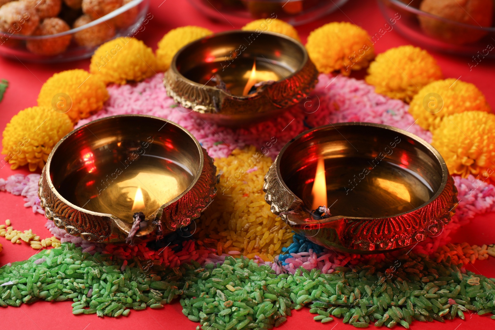 Photo of Happy Diwali. Diya lamps, colorful rangoli and flowers on red table, closeup