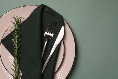 Photo of Stylish table setting. Plates, cutlery, napkin and rosemary on green background, top view with space for text