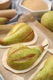Tray with raw dough and fresh pears on table, closeup
