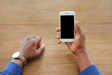Photo of African-American man holding mobile phone with blank screen in hand at table
