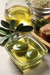 Photo of Fresh oil, ripe olives and green leaves on white wooden table, closeup