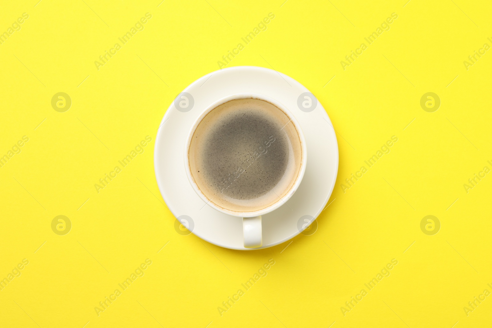 Photo of Aromatic coffee in cup on yellow background, top view