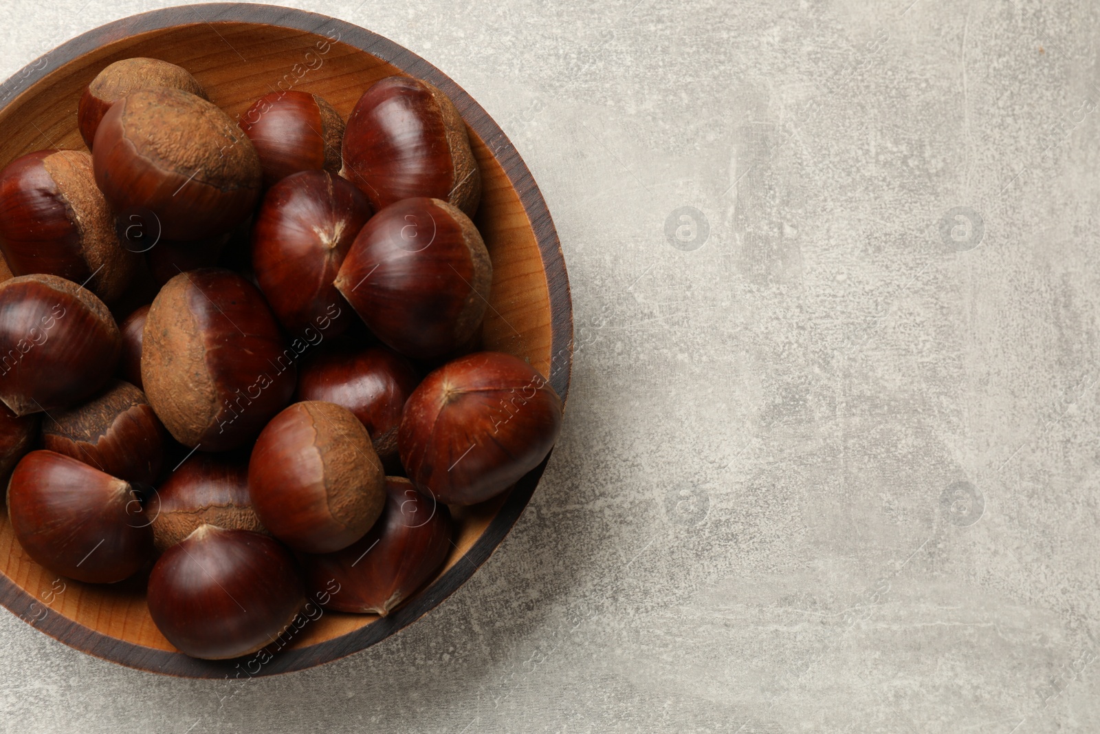 Photo of Roasted edible sweet chestnuts in bowl on light grey table, top view. Space for text