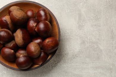 Roasted edible sweet chestnuts in bowl on light grey table, top view. Space for text